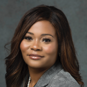 A professional headshot of Geraldine Montilus, with soft wavy hair, wearing pearl earrings and a pearl necklace, and a houndstooth-patterned blazer.