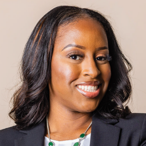 Close-up portrait of Sherline Lexime, with a warm smile, wearing professional attire and a necklace with green stones, exuding confidence and friendliness