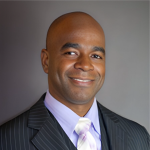 Portrait of Vedner Guerrier, MBA, LSSBB, with a gentle smile, wearing a pinstripe suit and a pastel tie.