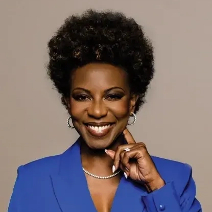 The image shows Tamara Rodriguez, a Board Member for 2024. She is smiling warmly, wearing a bright blue blazer and a pearl necklace. Tamara has a natural afro hairstyle and is posing with one hand gently touching her chin. The neutral beige background enhances her elegant and confident appearance.