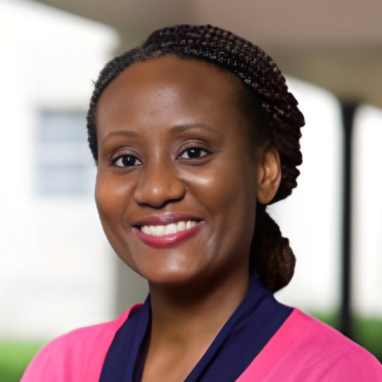 A professional headshot of Dr. Danna Demezier, who is smiling warmly. She has braided hair and is wearing a pink and navy outfit. The background is softly blurred, suggesting an indoor setting.