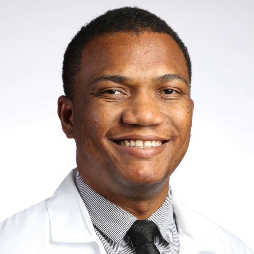 Portrait of Dr. Garly Saint Croix, a smiling male cardiologist wearing a white coat, striped shirt, and black tie.