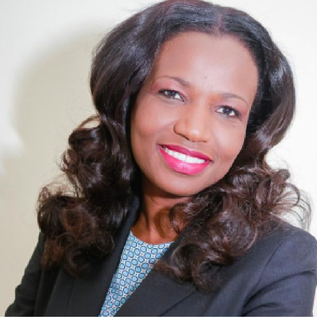 Portrait of former chair Lumana Joseph, smiling, with long, curly hair, wearing a dark blazer and a patterned blouse.