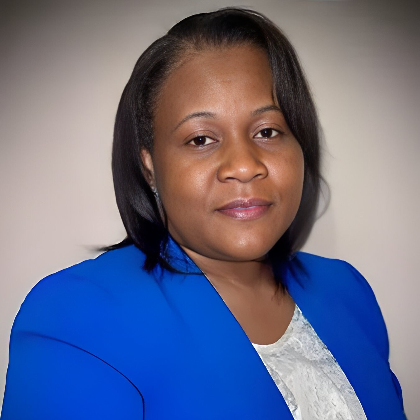 The image shows Melyn Bailer Joseph, a Board Member for 2024. She is wearing a blue blazer over a white blouse, with a calm and composed expression on her face. Melyn has shoulder-length black hair, and the background is a soft gradient that highlights her professional and poised appearance.