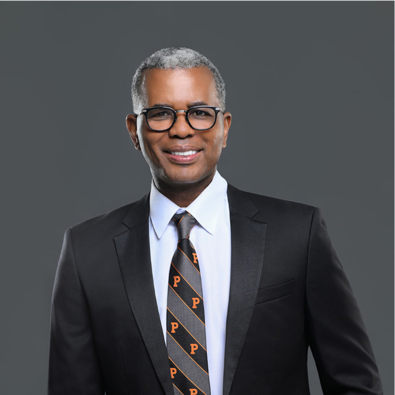 Portrait of former chair Prinston Jean-Glaude, smiling, wearing tailored suit, tie with P for Prinston on it.